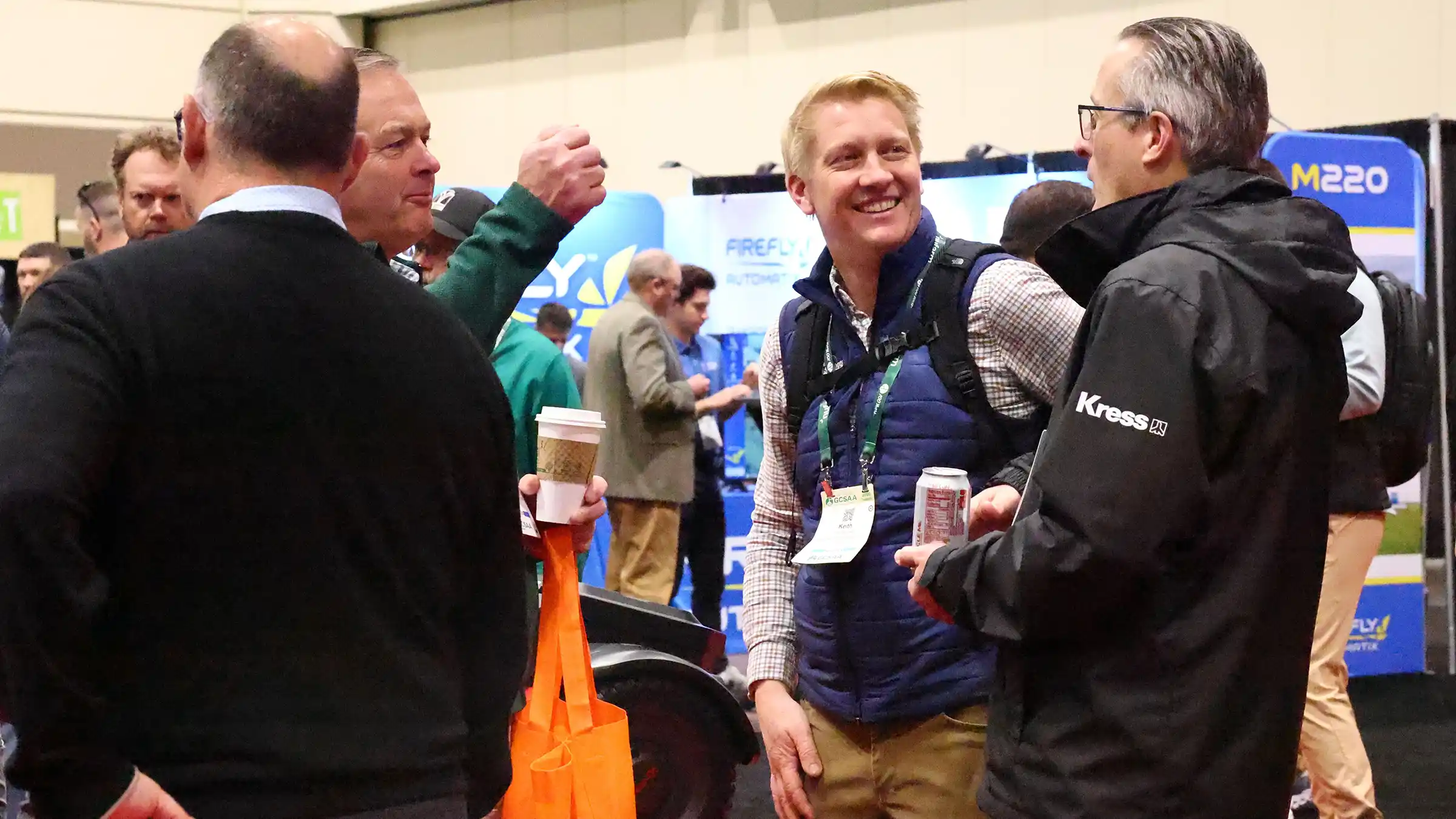 Attendees laughing and talking together in an aisle on the trade show floor.