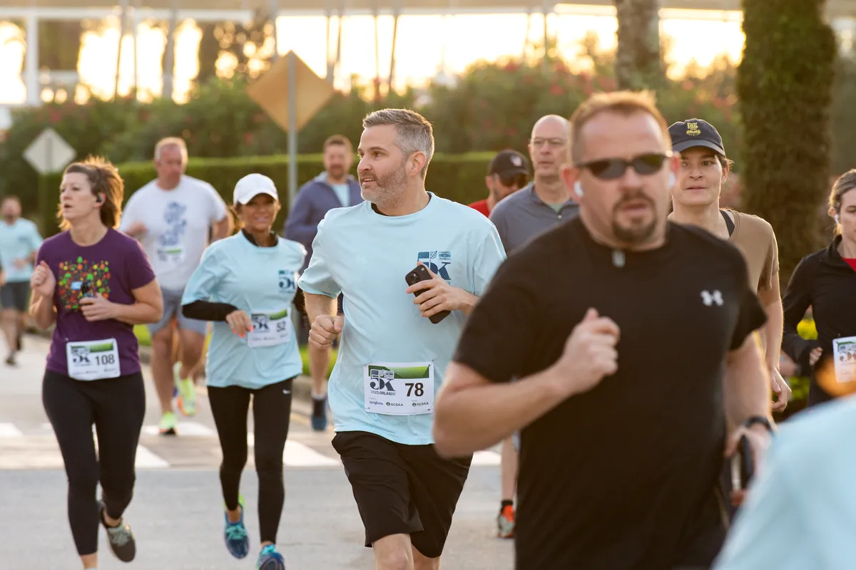 Runners in Health in Action 5K shirts and race bibs on the course at sunrise.