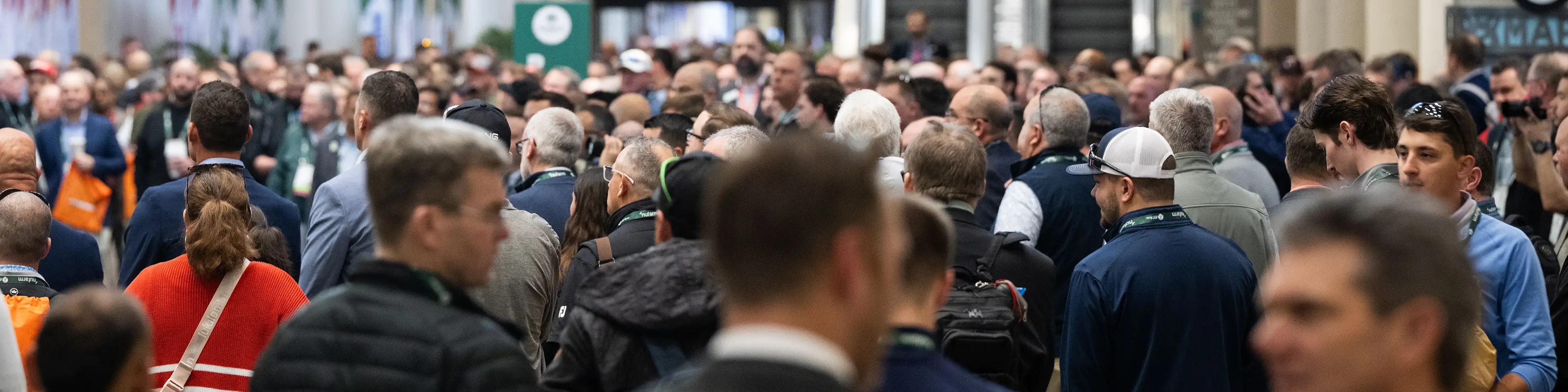 A crowd of attendees with conference badges filling a trade show aisle.