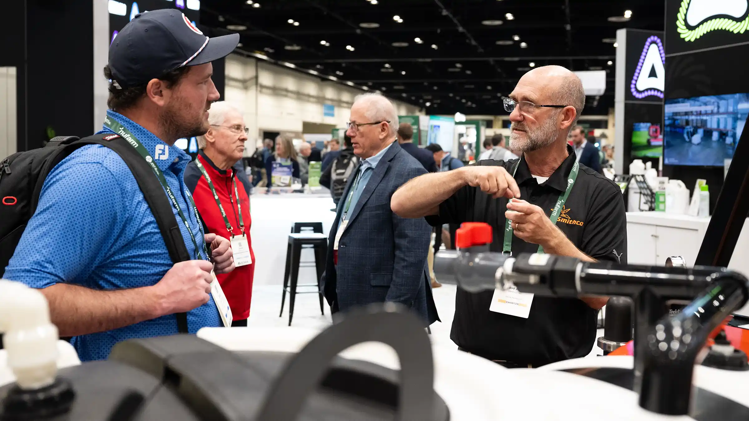 An exhibitor demonstrating a sprayer fitting to attendees at a trade show booth.