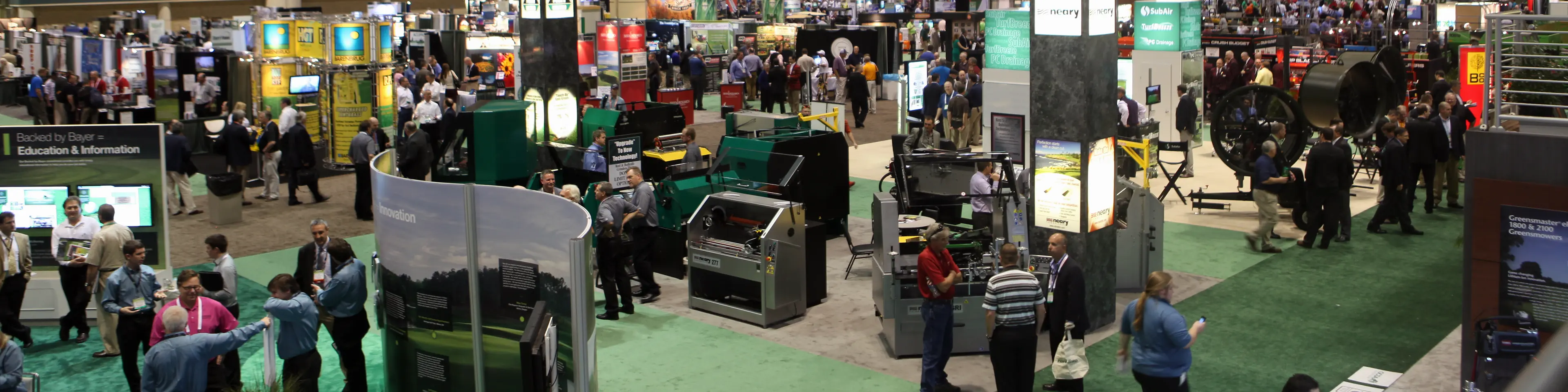 Attendees walking a busy aisle of exhibitor booths on the GCSAA trade show floor.